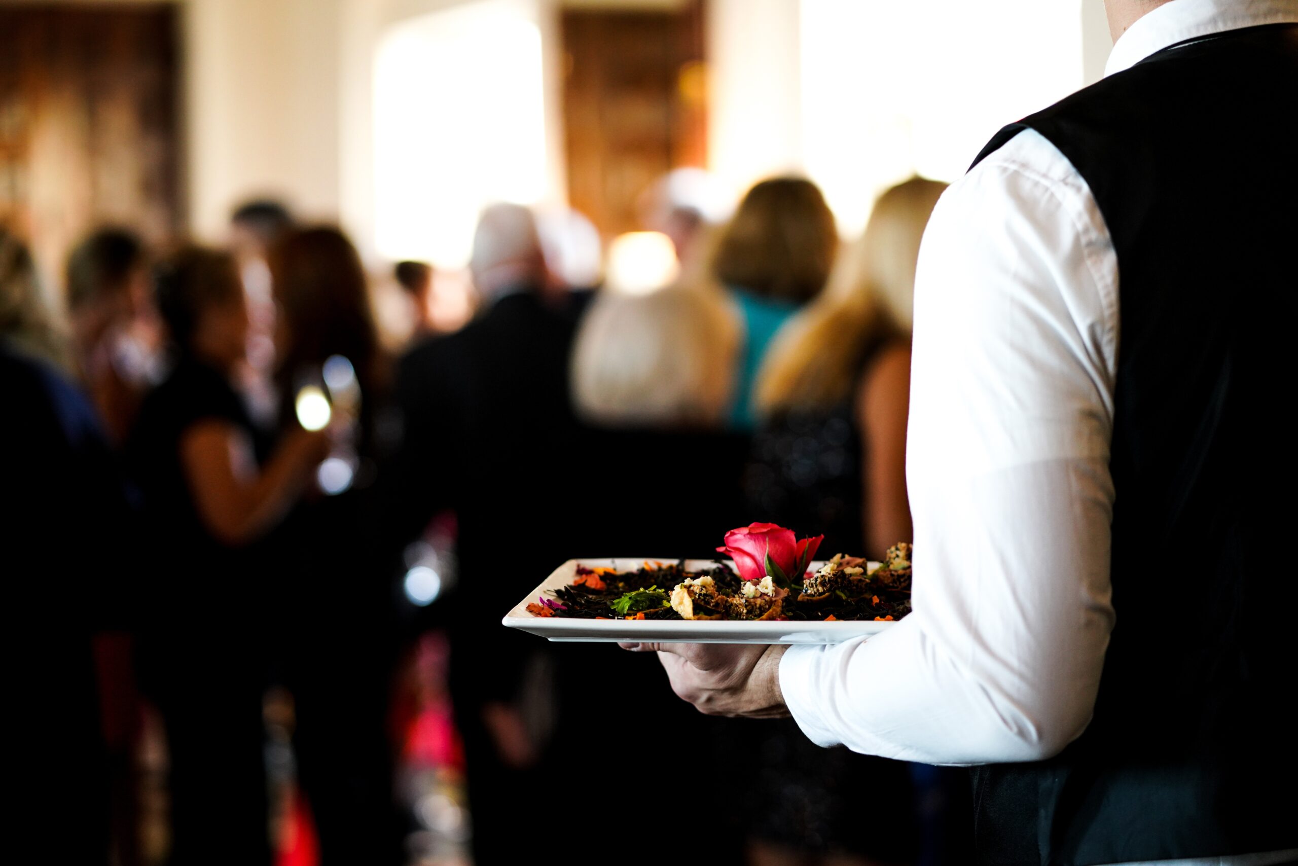 Closeup shot of a waiter’s arm carrying a plate of a dish with a pink rose in it